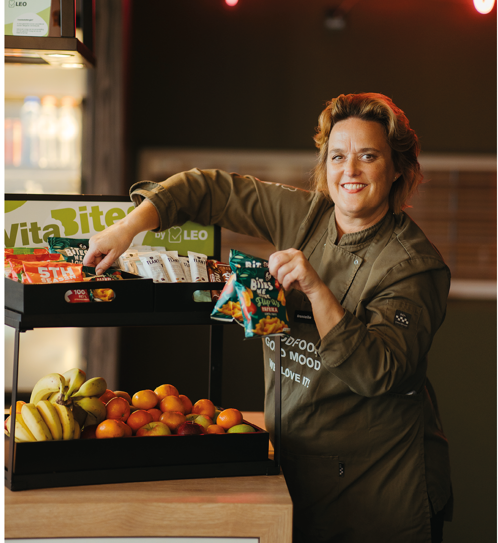 A woman in a green coat is smiling and holding a box of snacks. AI generated content