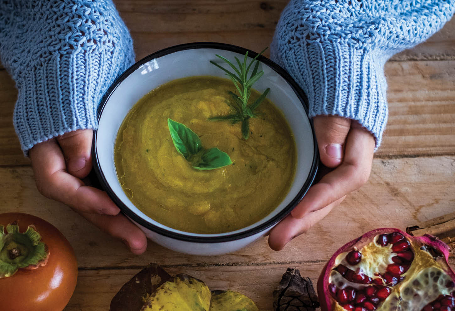 Above view of woman hands holding warm healthy autumn winter soup food to have lunch alone. Pommegranate and vegetables diet nutrition concept. wooden rustic table. Health people lifestyle