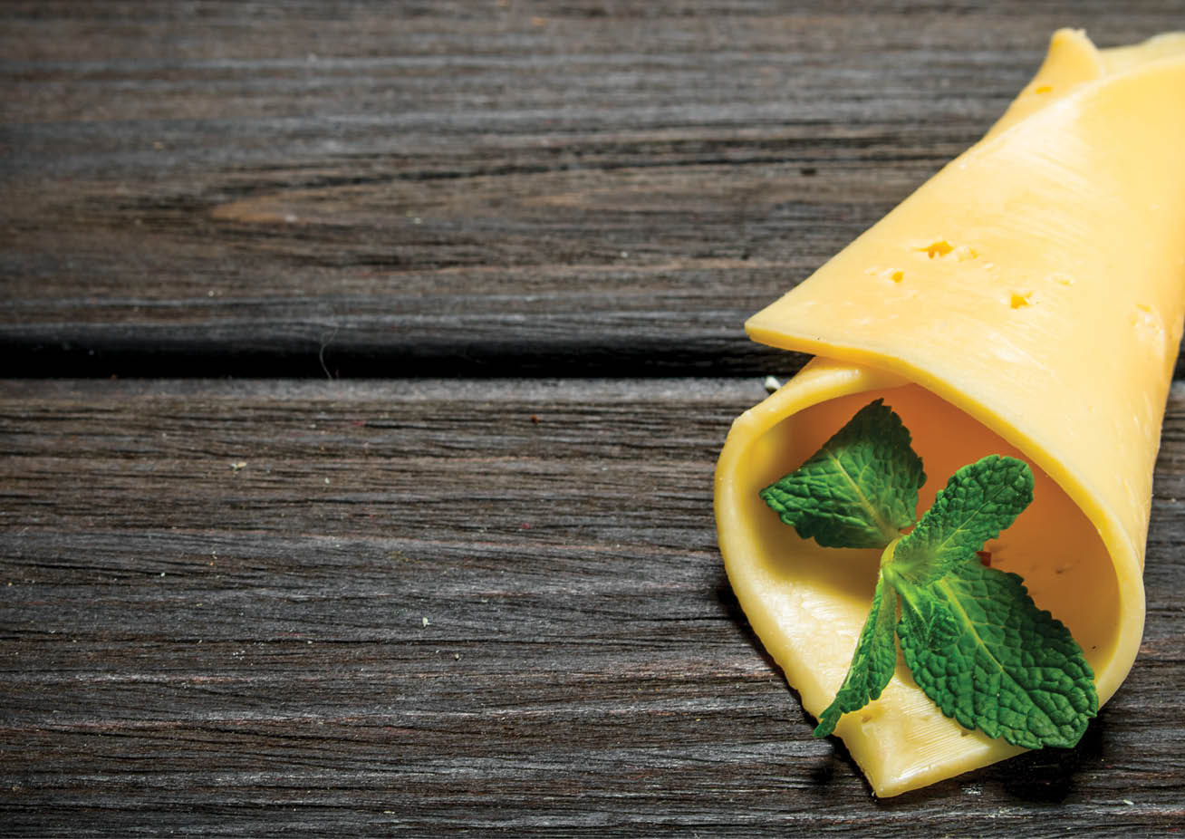 Thin slices of cheese with a branch of mint. On a wooden background.