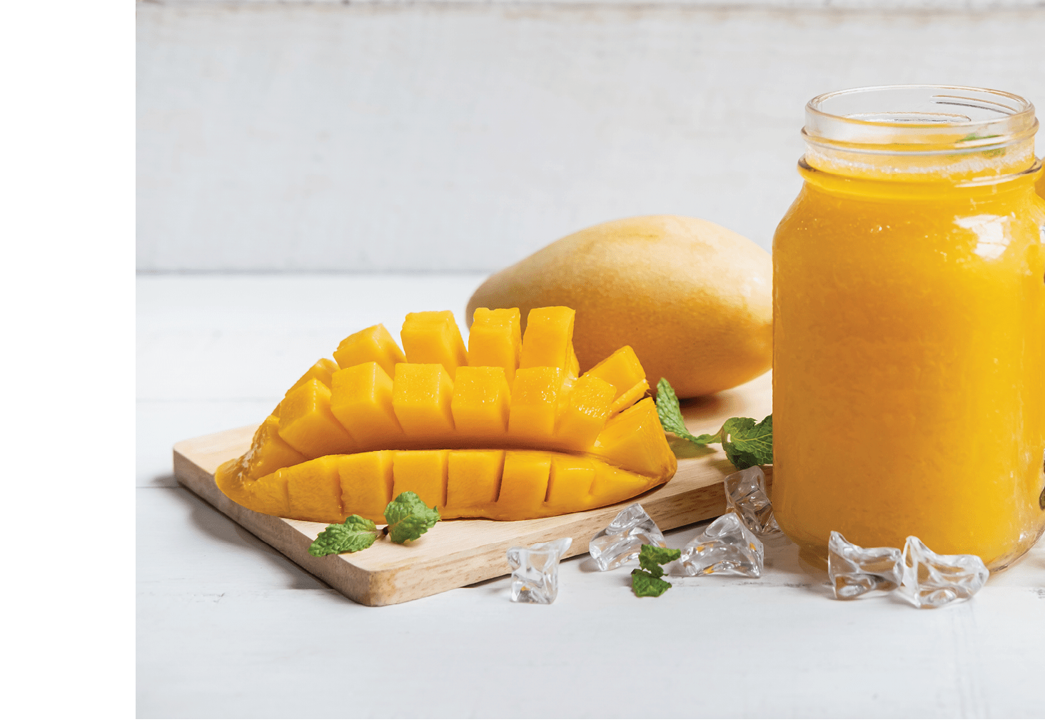 Refreshing mango smoothies in glass with ripe mango on white wooden table
