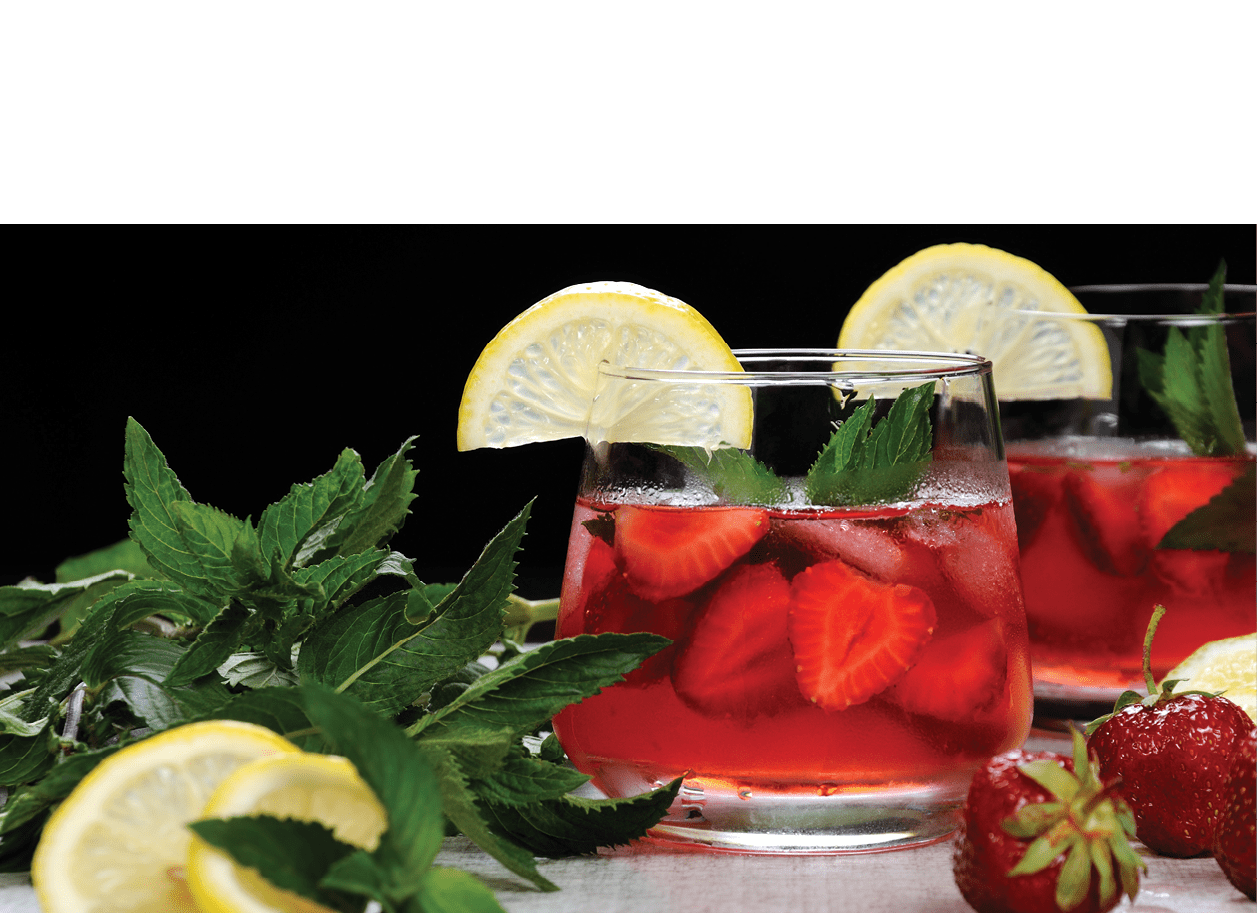 A glass of chilled strawberry lemonade, mint leaves, a slice of lemon with ice