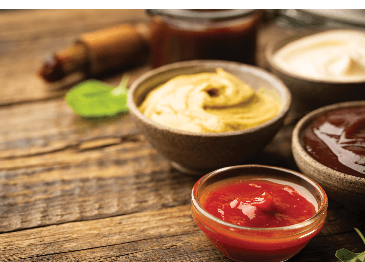 Classic set of sauces, American yellow mustard, ketchup, barbecue sauce, mayonnaise on wooden background, top view with copy space.