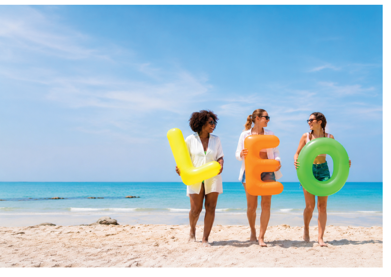 Three women standing on a beach with a large letter L. Description generated by AI