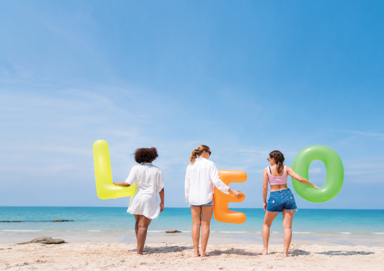 Four women standing on a beach, each holding a letter of the word Leo. Description generated by AI