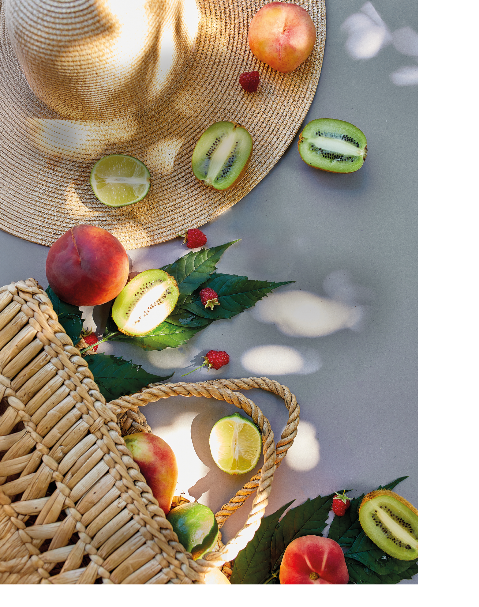 Flat lay of Straw Hat And Bag With Fruits raspberry, peach, kiwi, lime on grey background in sunlight, summer time. Grocery concept, copy space, top view.