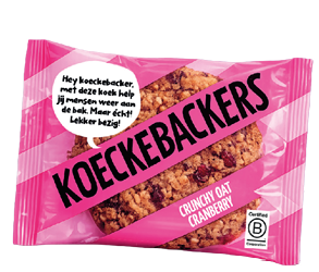 A pink package labeled KoekeBackers contains a crunchy oat cranberry cookie with a speech bubble in Dutch promoting the cookie's help in keeping people busy. Description generated by AI