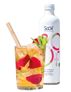 A glass filled with iced tea garnished with red rose petals and a green leaf sits in front of a white bottle labeled Soof with a wooden straw inside the glass. Description generated by AI