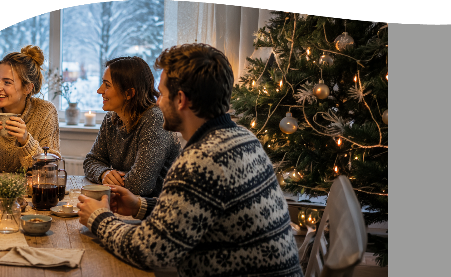 Three adults wearing cozy sweaters are sitting around a wooden table drinking coffee and chatting near a decorated and lit Christmas tree in a warmly lit room with a snowy window view. Description generated by AI
