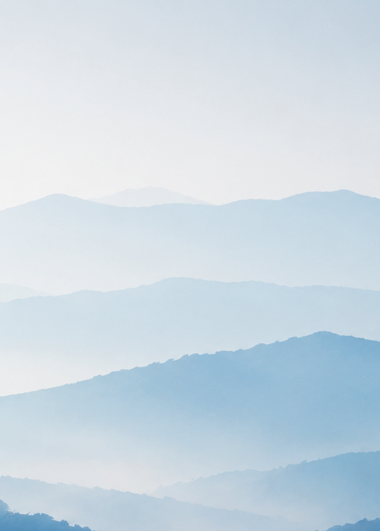 Layers of misty blue mountains fade into the distance under a pale sky. Description generated by AI