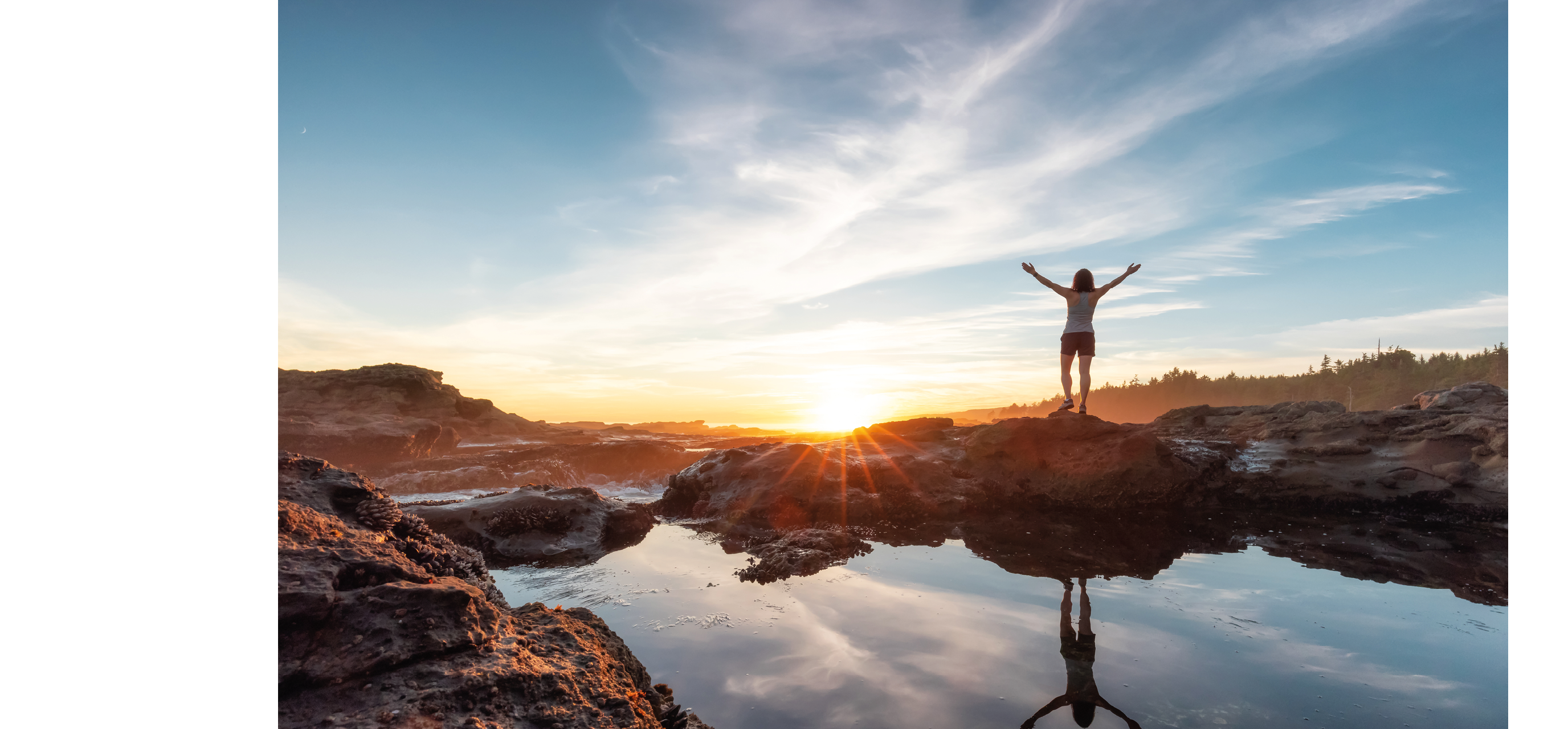 A woman standing on a rock with her arms raised. Description generated by AI