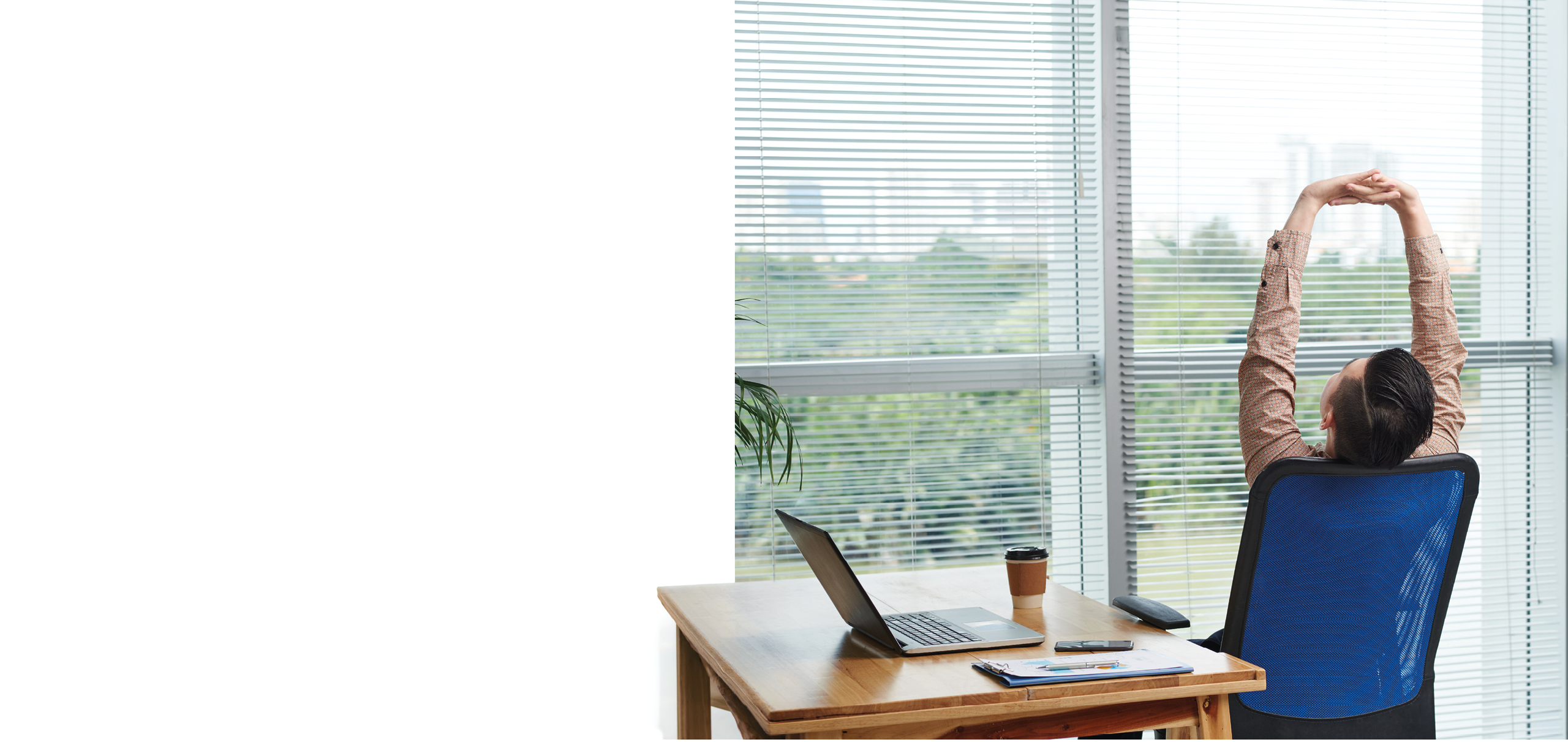 A woman is sitting in a blue chair at a desk with a laptop and a cup of coffee. Description generated by AI