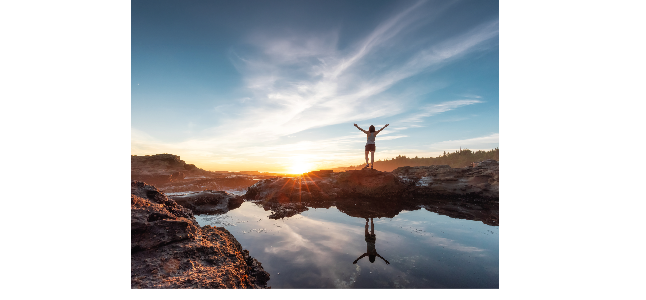 A woman standing on a rock with her arms raised. Description generated by AI